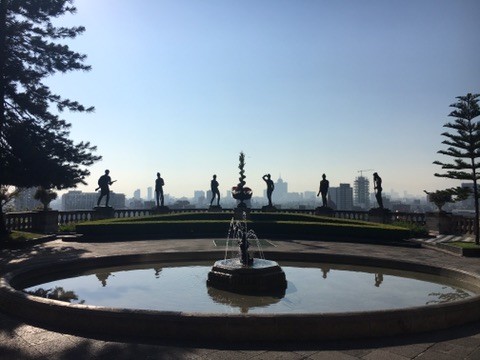 A circular fountain and statues silhouetted against the sky