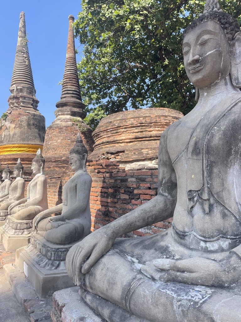 Seated Buddha statues beside brick stupas beneath a blue sky