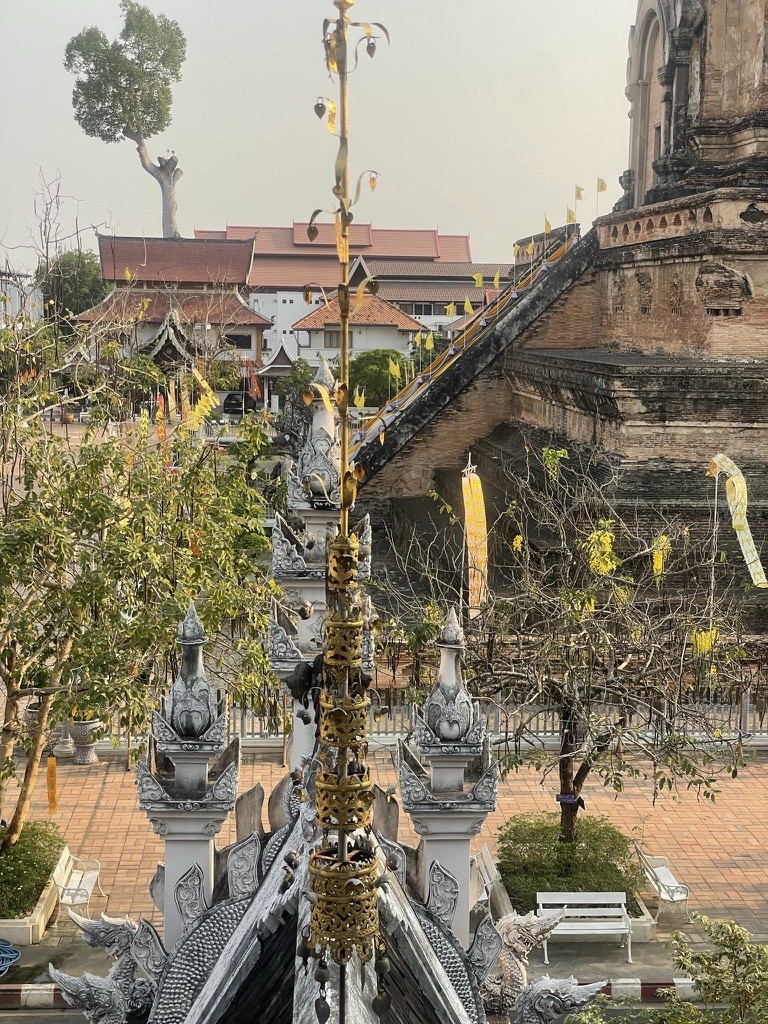 Decorated temple spires beside a weathered stone stupa and leafy trees
