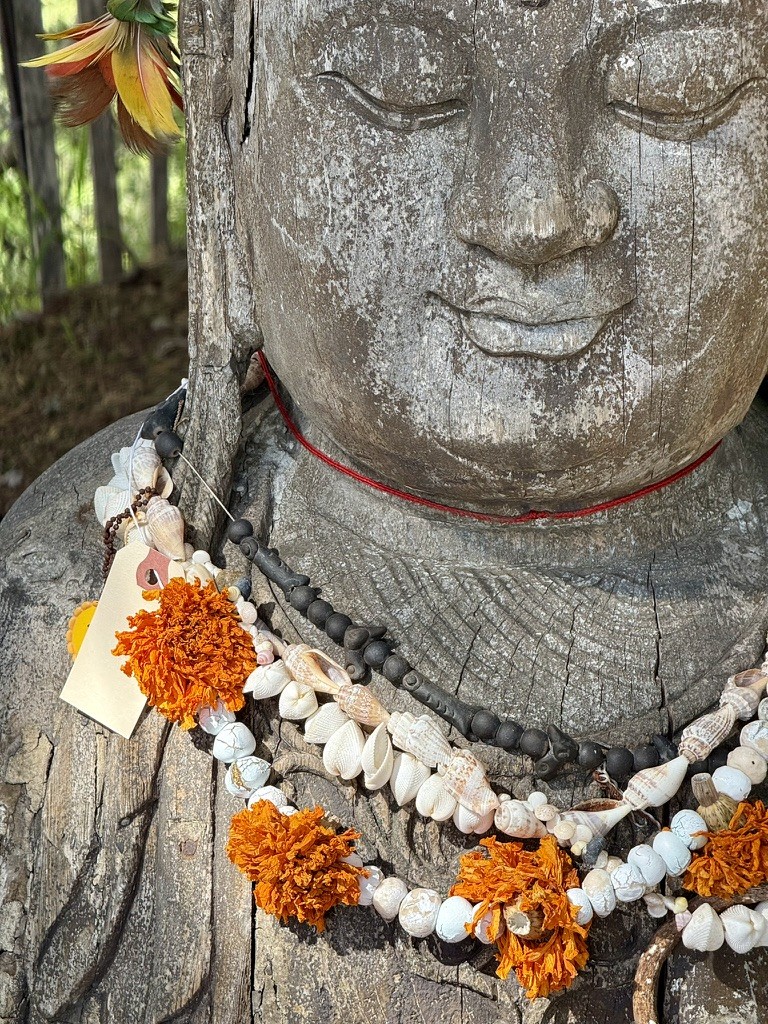 A weathered Buddha statue draped in white and orange flower garlands