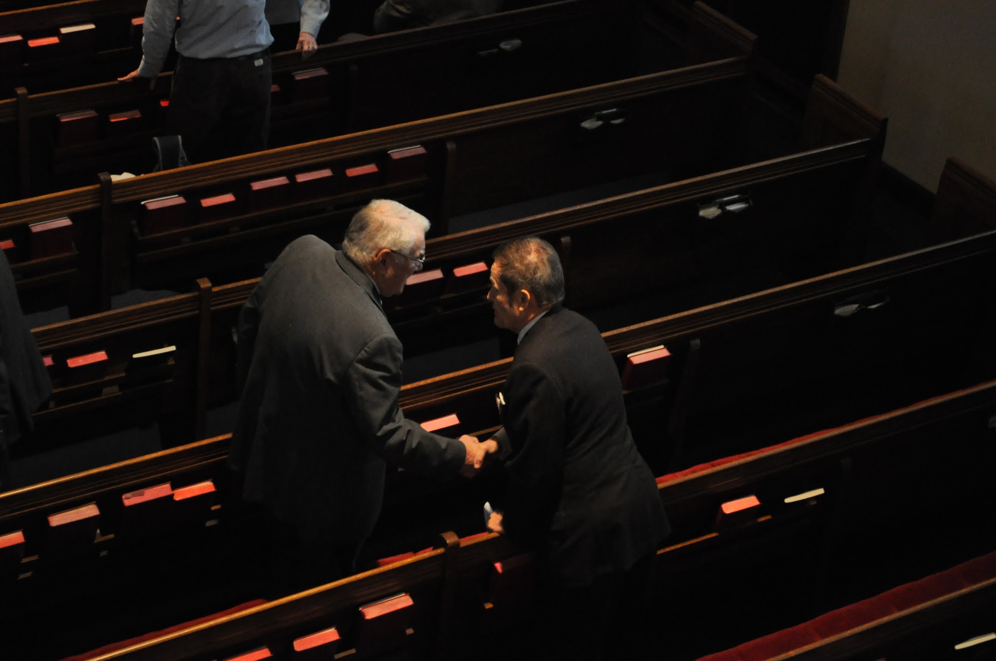 Two men shaking hands among dark wooden church pews