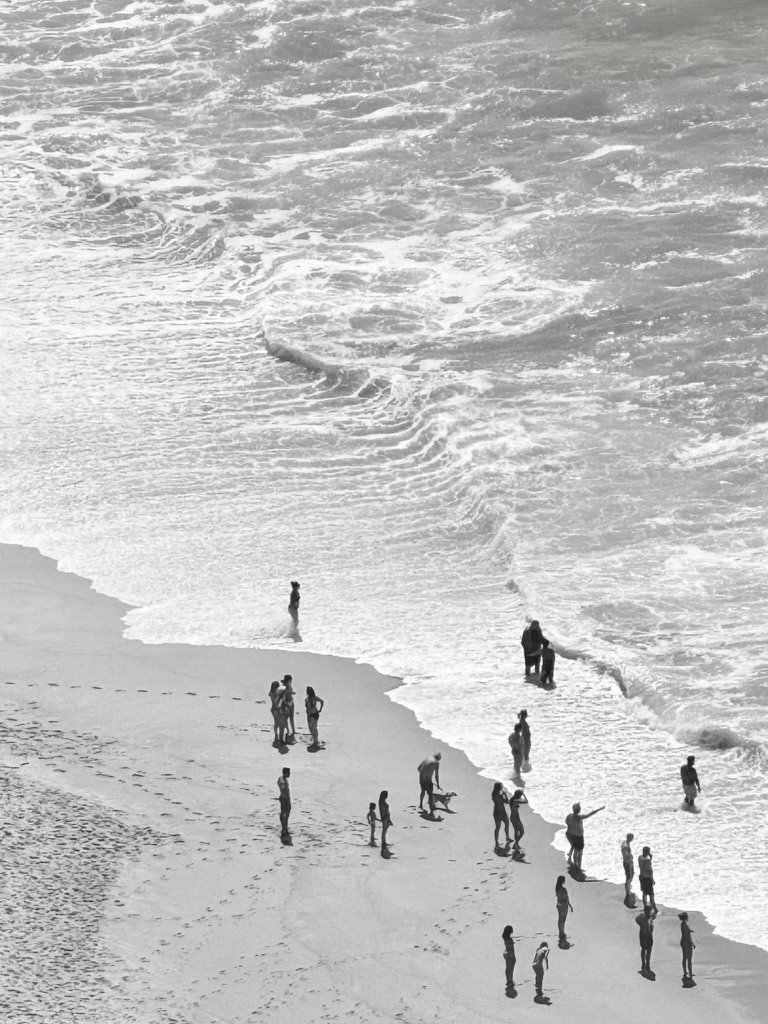 A black-and-white view of people standing along the surf