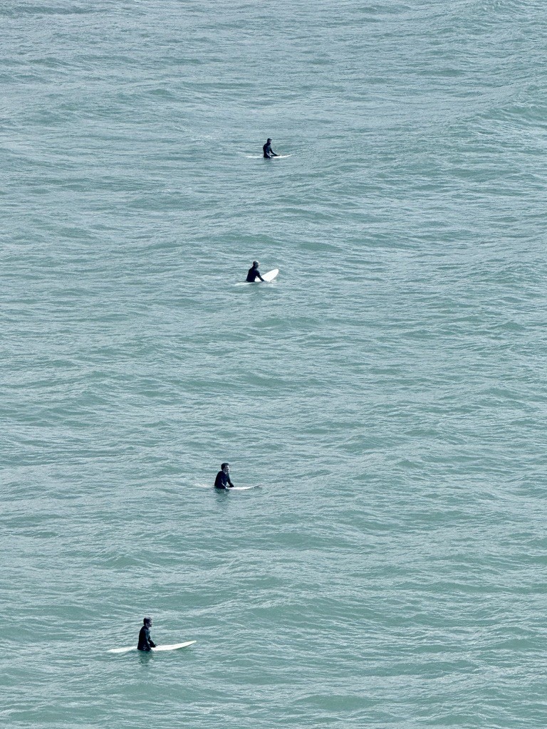Surfers spaced across blue-green water, viewed from above