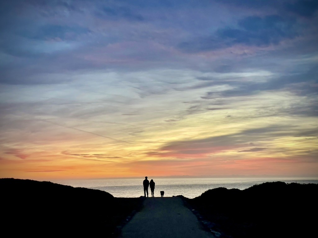 Two people silhouetted beneath a colorful sunset sky