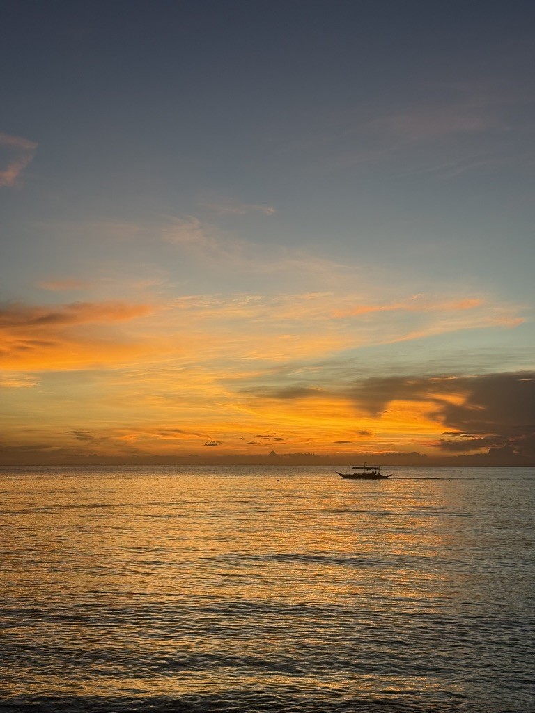 A boat on calm water beneath orange sunset clouds