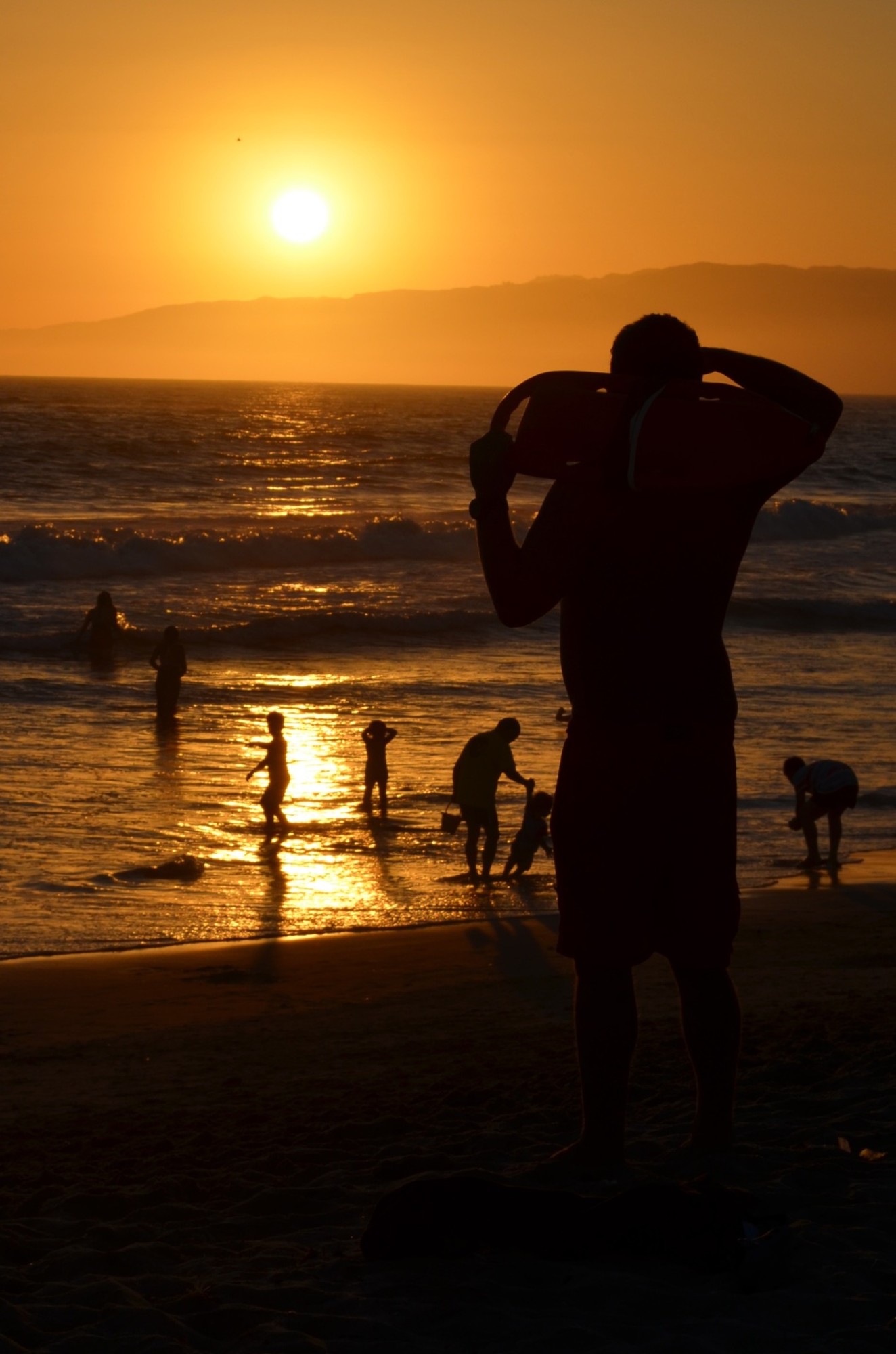 People silhouetted on a beach beneath an orange sunset